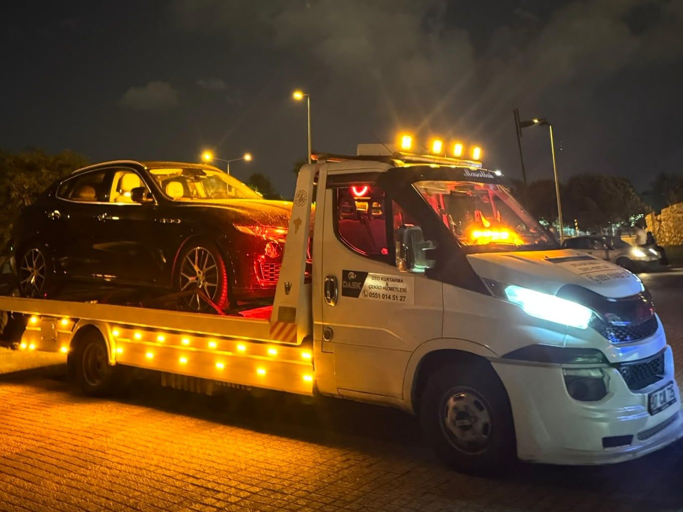 Gece tepe lambaları yanan Dask Oto Kurtarma çekicisi, kasasında siyah otomobil